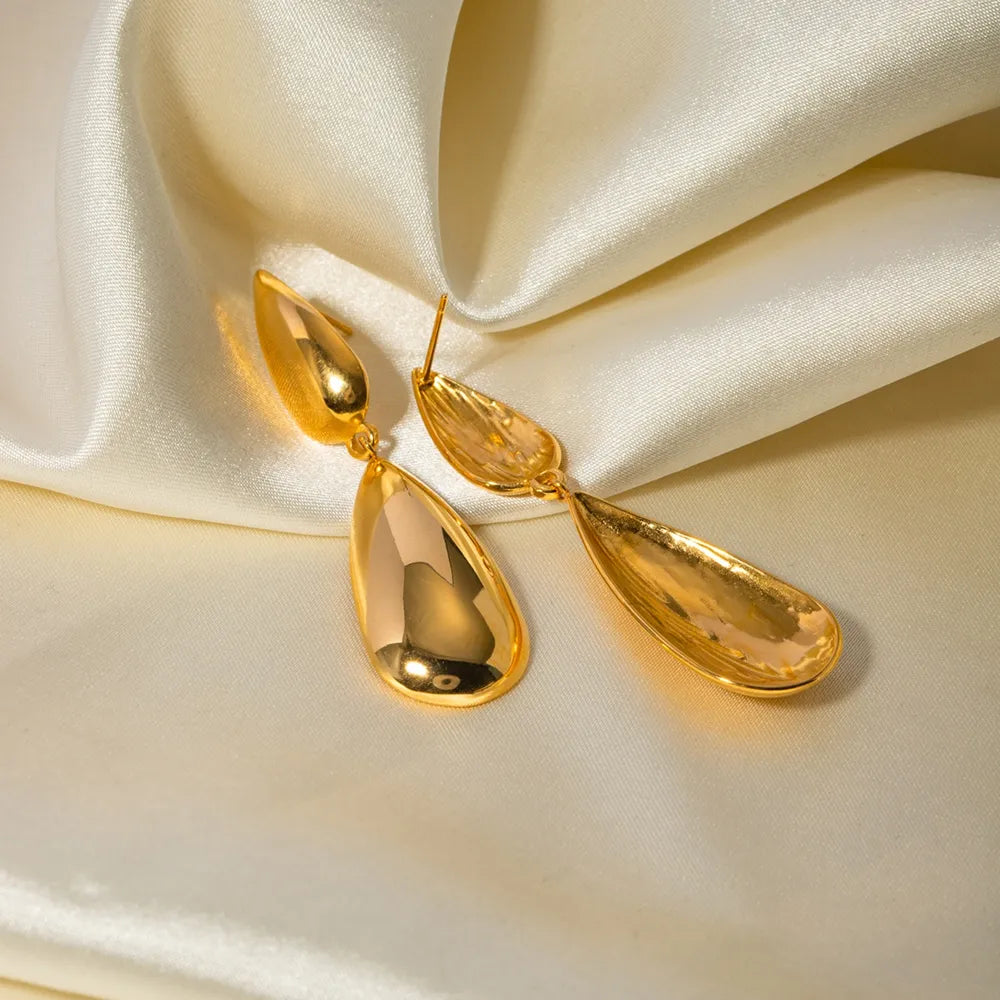 Gold teardrop dangle earrings with a polished finish on a satin background.