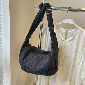 Black quilted crescent shoulder bag with adjustable strap and pleated detail.