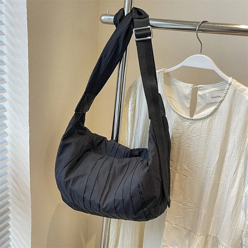 Black quilted crescent shoulder bag with adjustable strap and pleated detail.