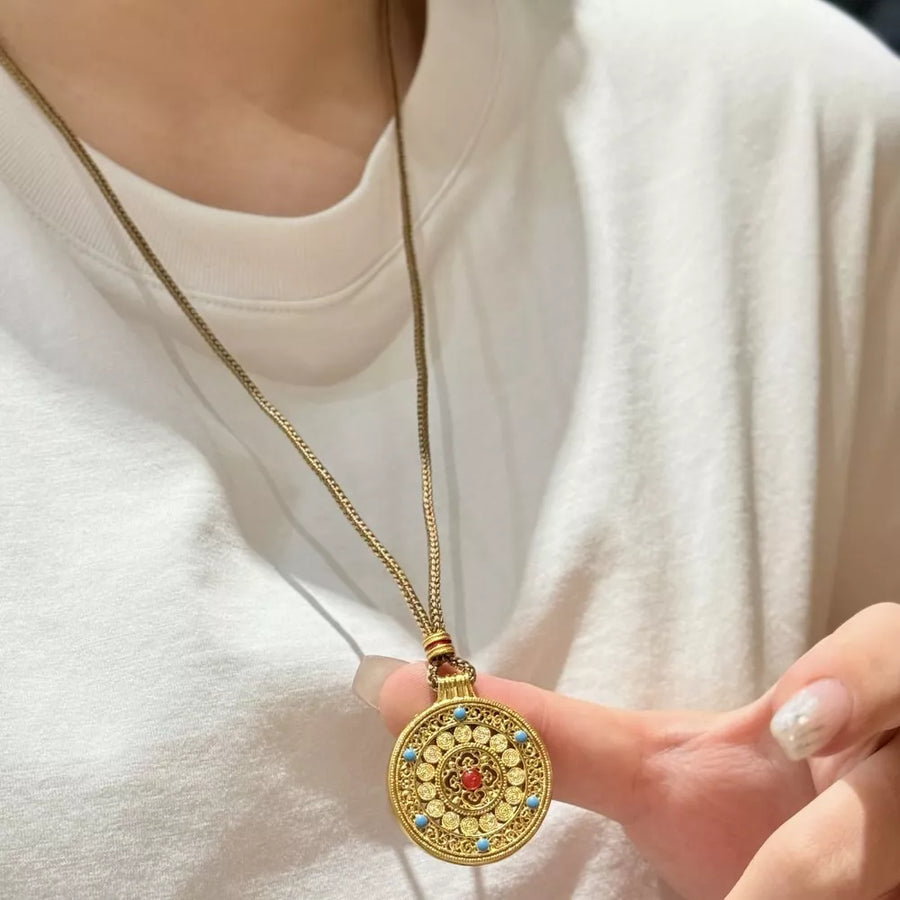 Gold-plated round pendant necklace with red and blue stone accents on a delicate chain.