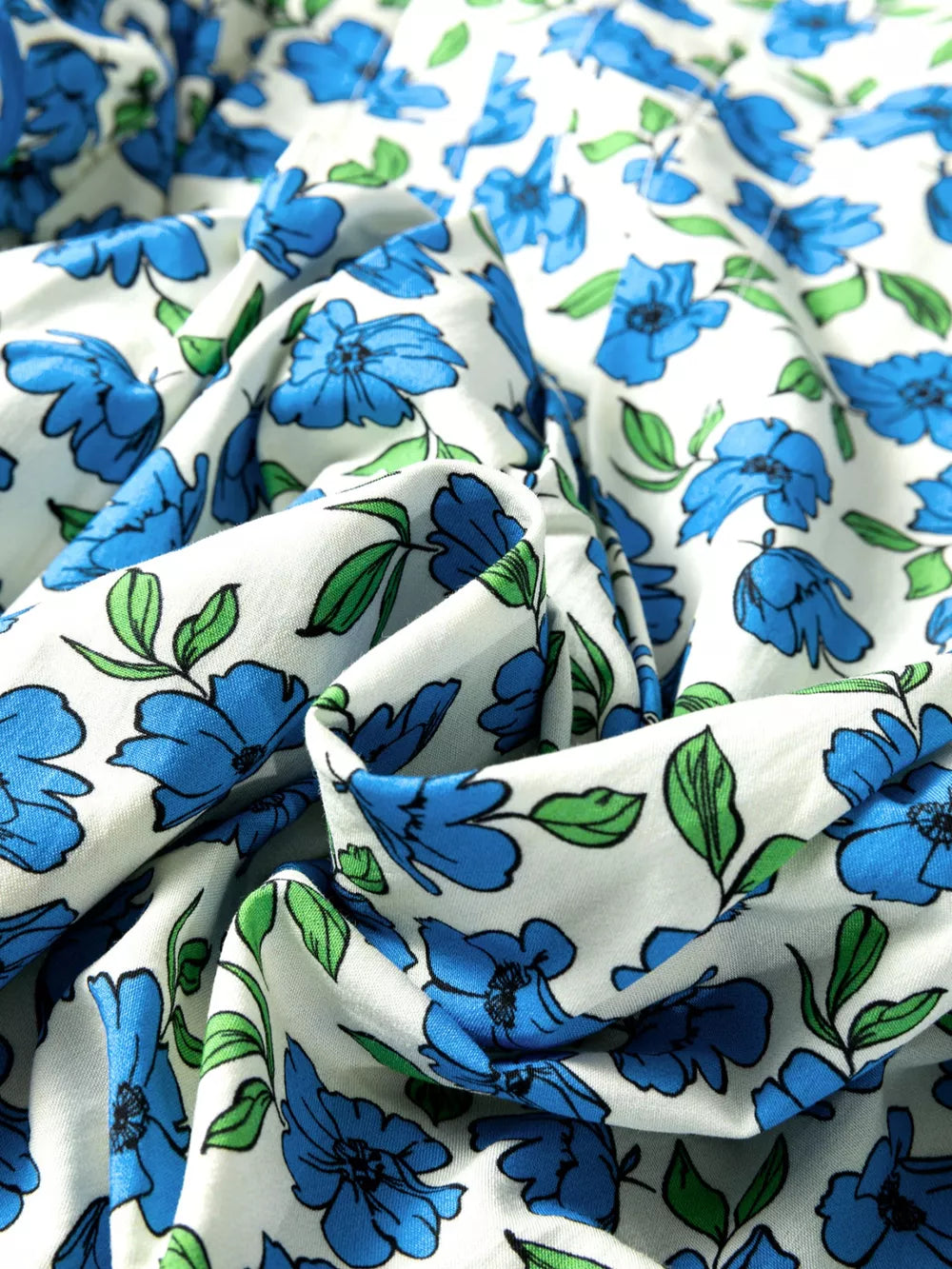 Floral ruffle sleeve tie-neck shirt in white with blue flowers and green leaves.