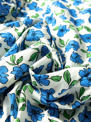 Floral ruffle sleeve tie-neck shirt in white with blue flowers and green leaves.