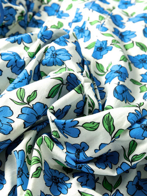 Floral ruffle sleeve tie-neck shirt in white with blue flowers and green leaves.