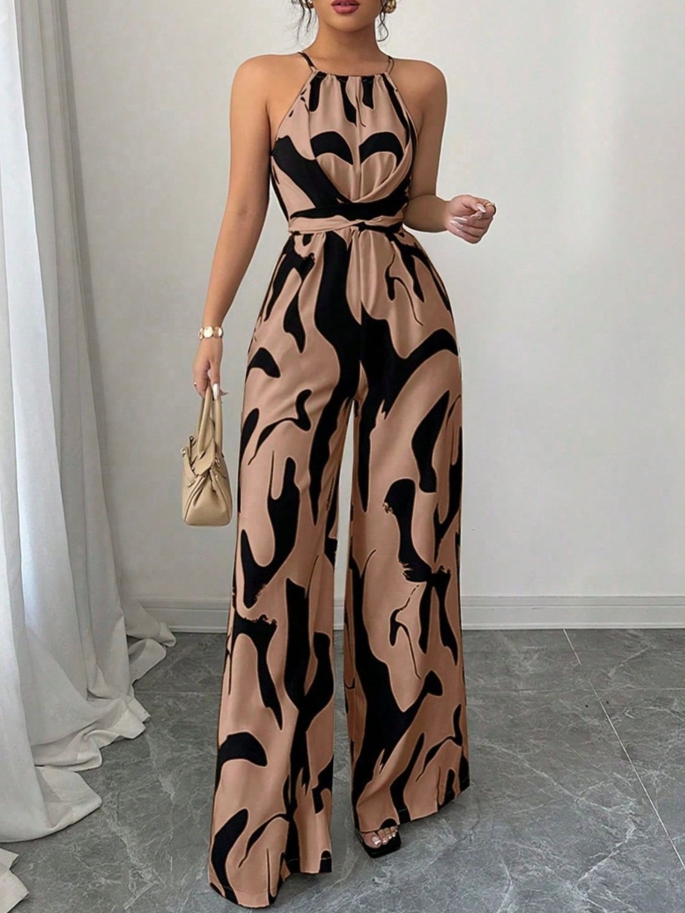 Elegant wide-leg jumpsuit in tan with abstract black print, halter neck, and draped bodice.