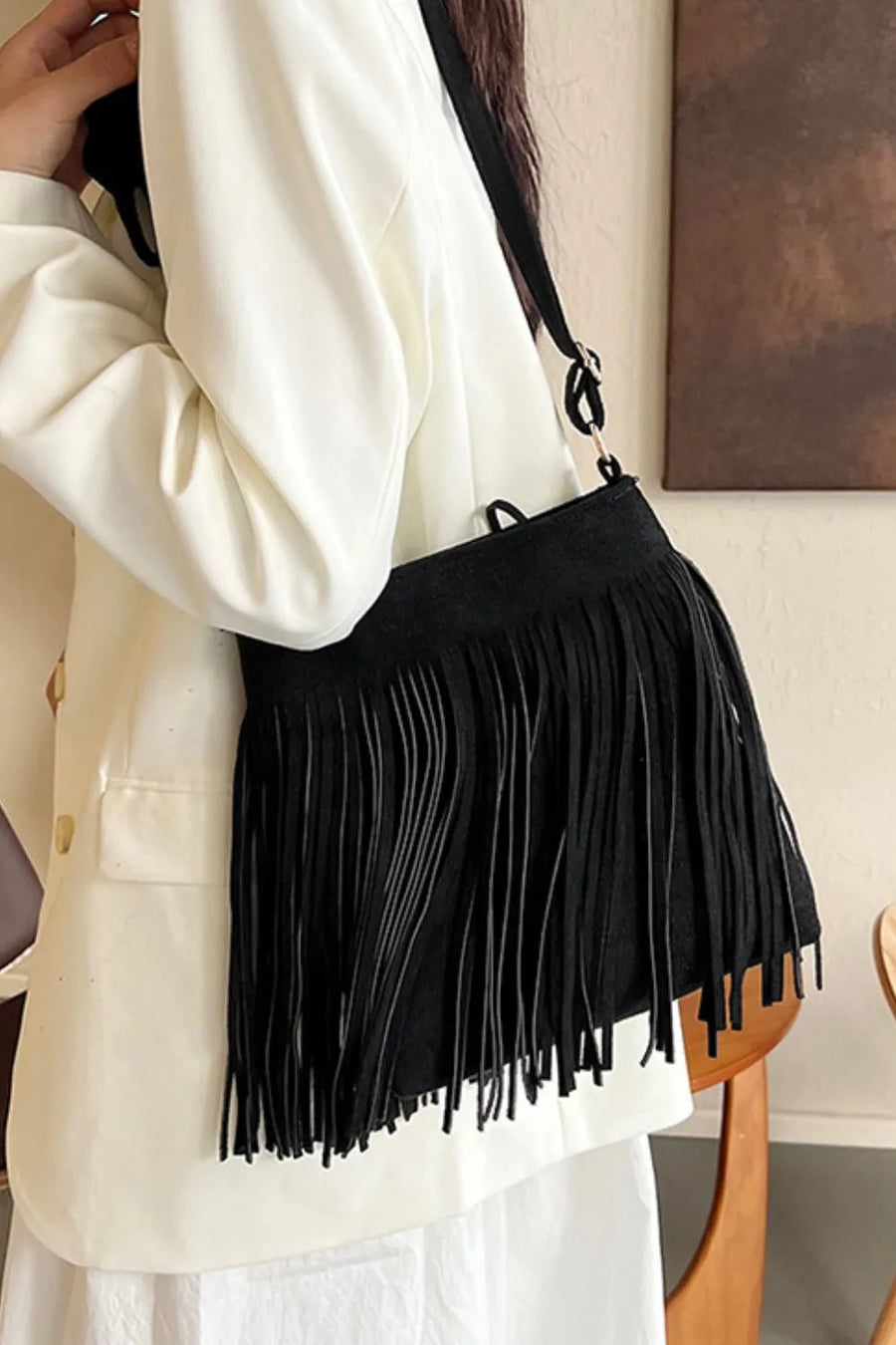 Black suede crossbody bag with long fringe detail and adjustable strap.