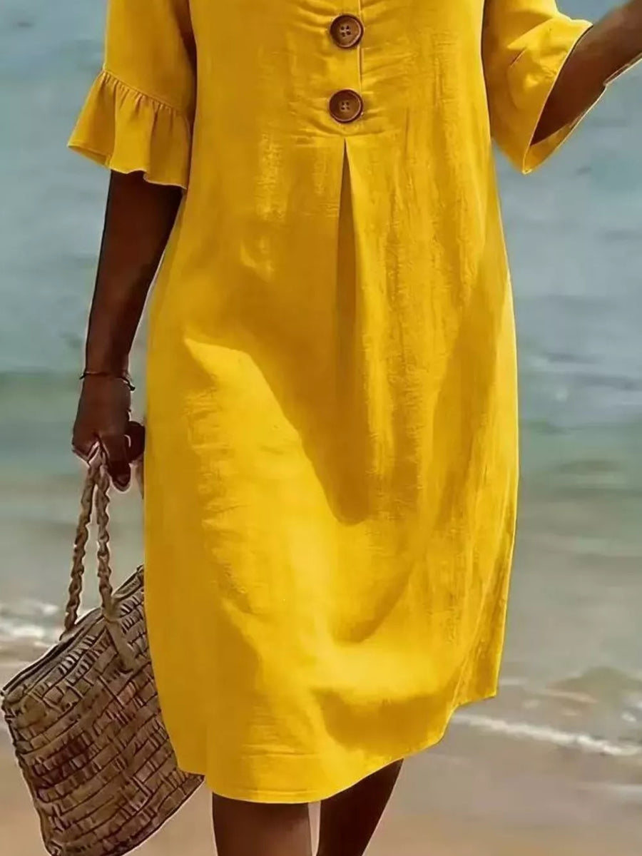 Yellow ruffled sleeve button detail dress with a pleated front, styled with a straw bag.