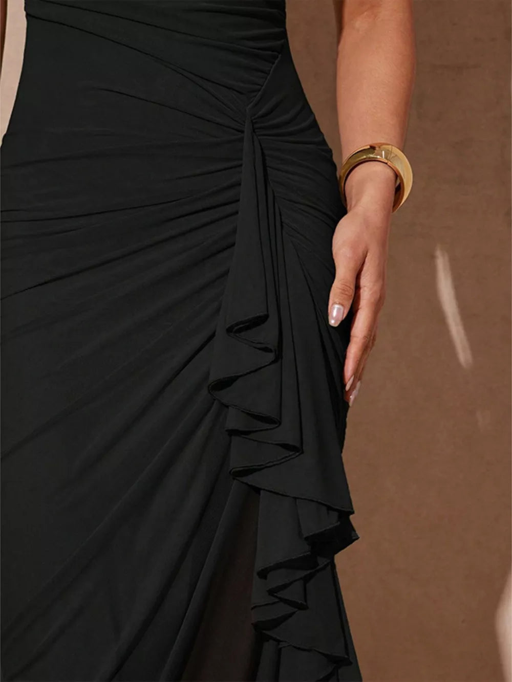 Black ruched dress with cascading ruffle detail and a gold cuff bracelet.
