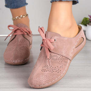 Pink perforated slip-on mules with lace-up detail and cutout heel.