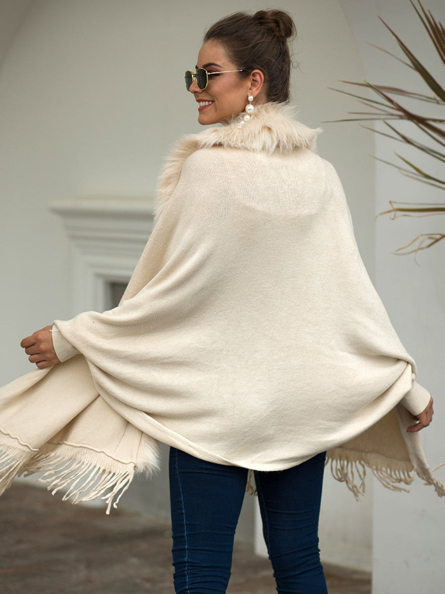 Ivory knit cape with faux fur trim and fringe detailing.