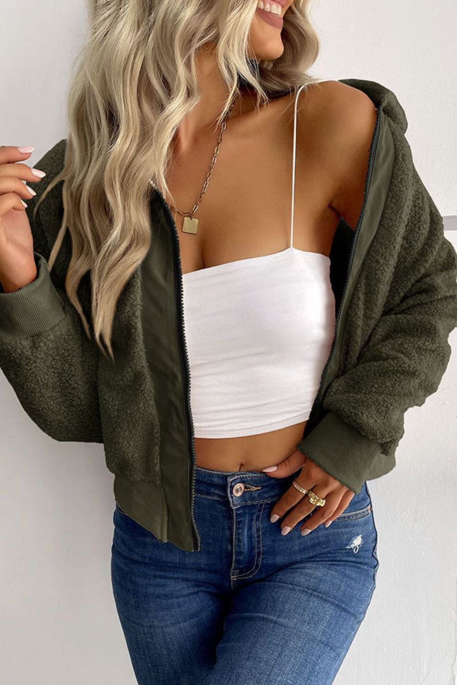 Green teddy fleece bomber jacket with collared neck and zip front, styled with a white tube top and jeans.