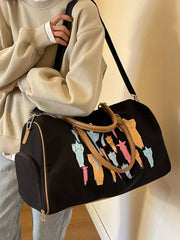 Black canvas duffle bag with colorful star design and tan handles.