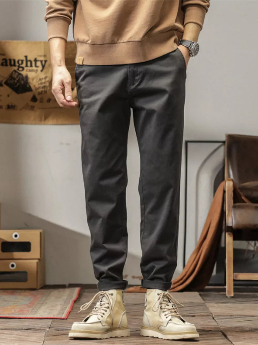 Men's dark gray slim fit ankle pants with cuffed hems, styled with a tan sweatshirt and boots.