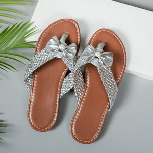 Silver bow-embellished flat sandals with woven straps and pearl detail.