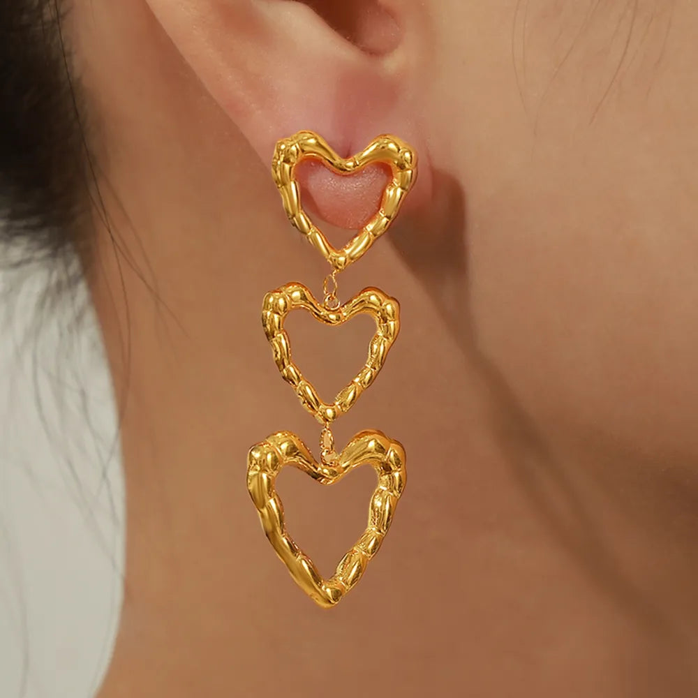 Gold triple heart drop earrings with textured detail.