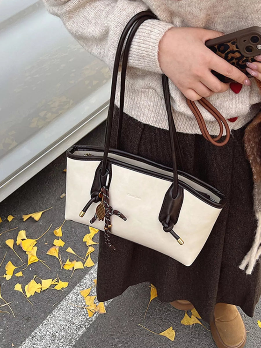 Vintage-inspired beige leather shoulder bag with dark brown trim and a playful lizard charm.