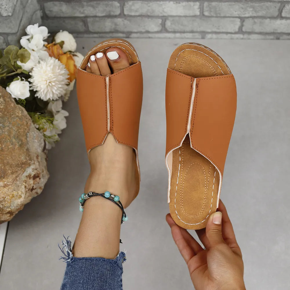 Asymmetrical vegan leather slides in caramel with white stitching and a pointed toe.