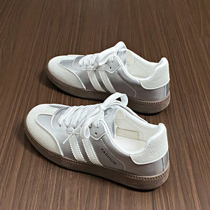 Silver leather sneakers with white laces and branding detail.