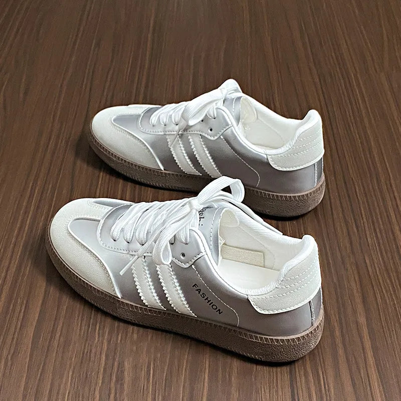 Silver leather sneakers with white laces and branding detail.