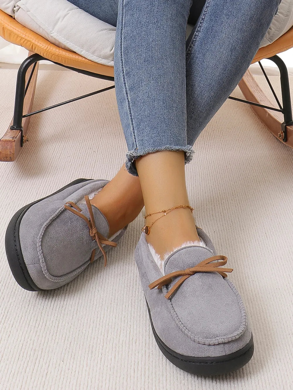 Gray suede moccasin slippers with white lining and bow detail.