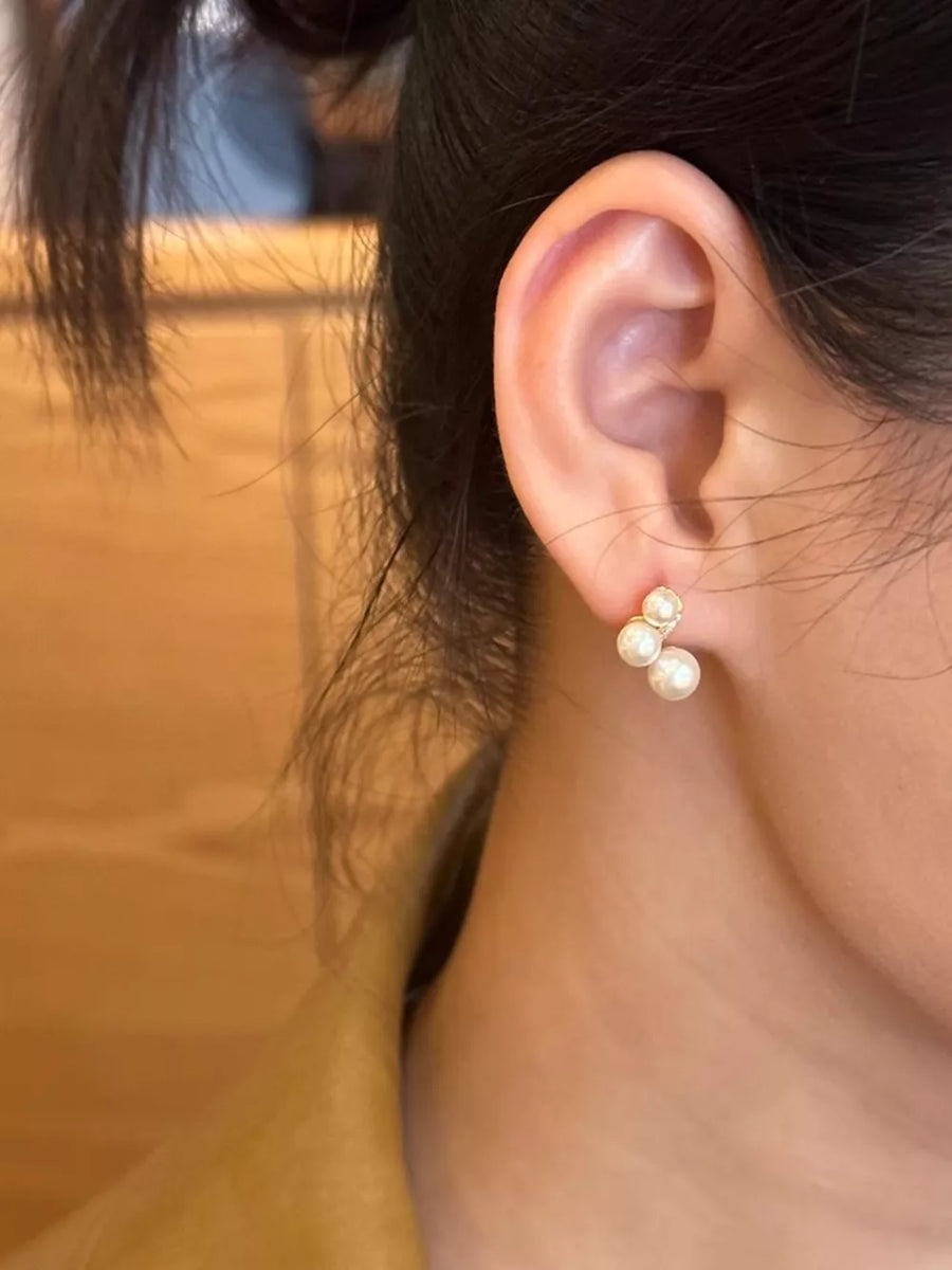 Elegant gold pearl cluster earrings with three small pearls on an adult woman's ear.