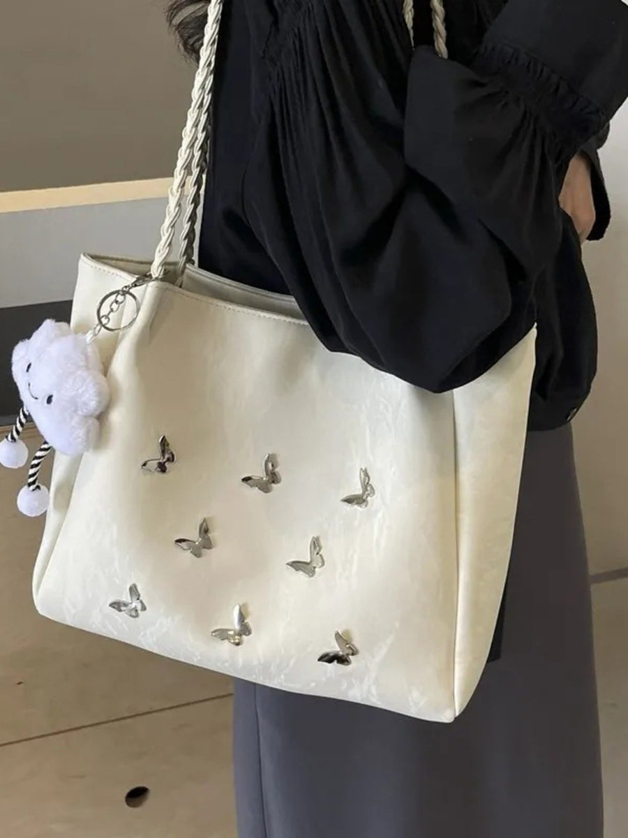 Cream shopper bag with braided handles and butterfly embellishments, featuring a cloud charm.