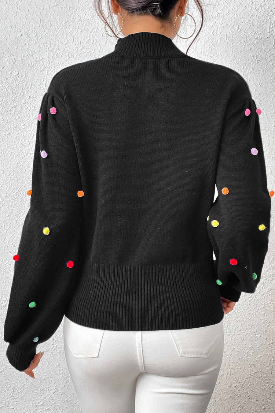 Black blouson sweater with colorful pom-pom embellishments on the sleeves.