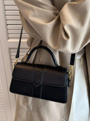 Chic small black top handle shoulder bag with gold hardware and a strap.
