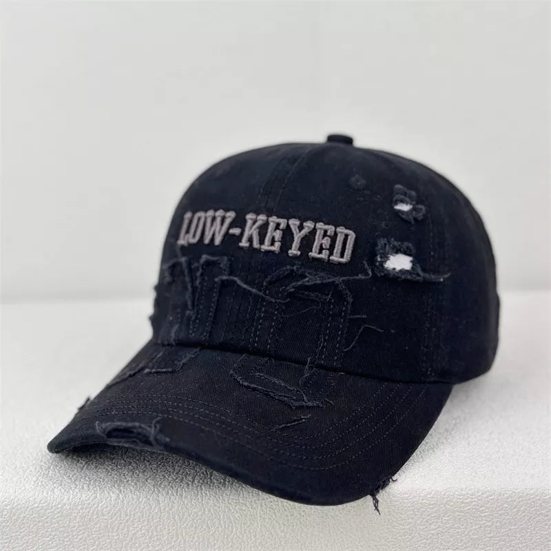 Black distressed baseball cap with embroidered LOW-KEYED text and frayed details.