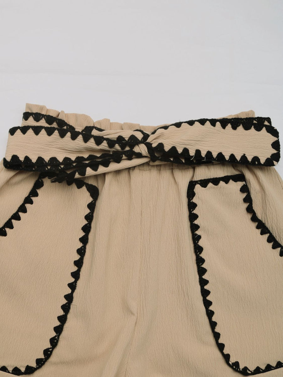 Tan paperbag shorts with scalloped black trim and a tie waist.