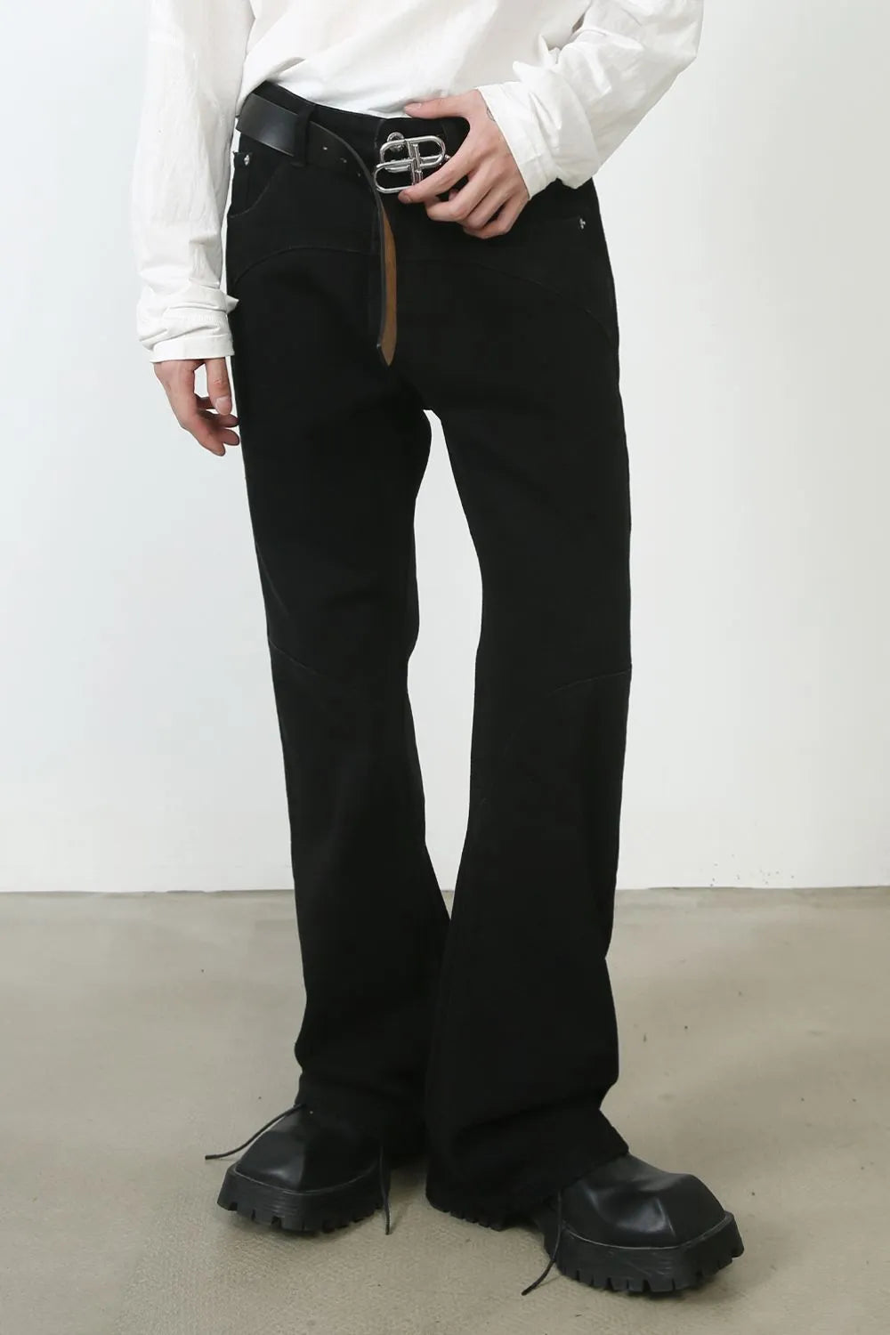Black denim trousers with flared leg and seam detail, styled with a belt.