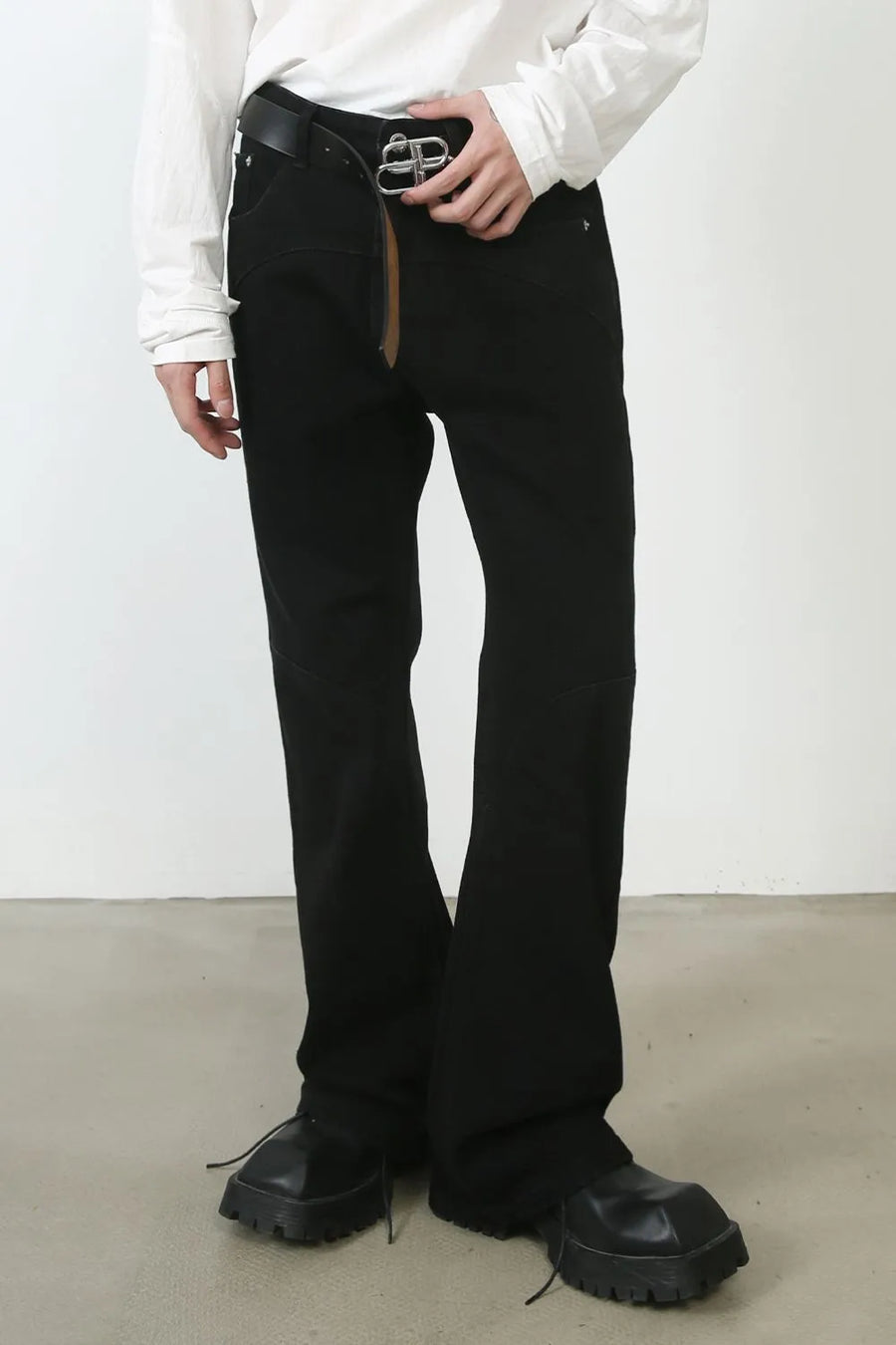 Black denim trousers with flared leg and seam detail, styled with a belt.