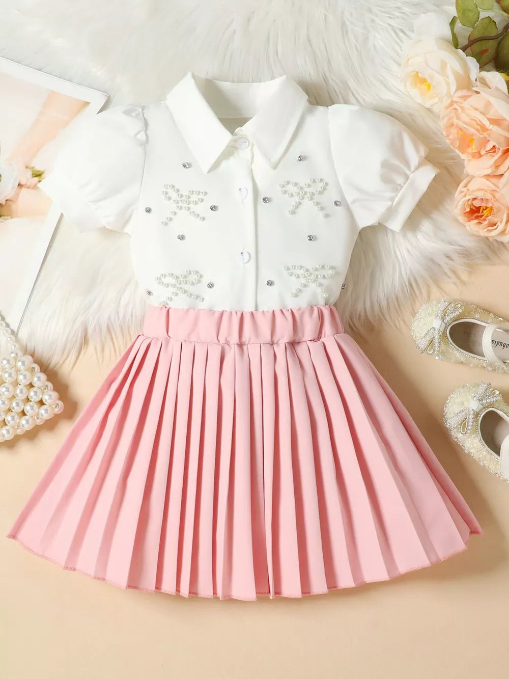 Girls' white bow-embellished top with puff sleeves and pink pleated skirt duo.