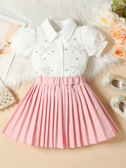 Girls' white bow-embellished top with puff sleeves and pink pleated skirt duo.