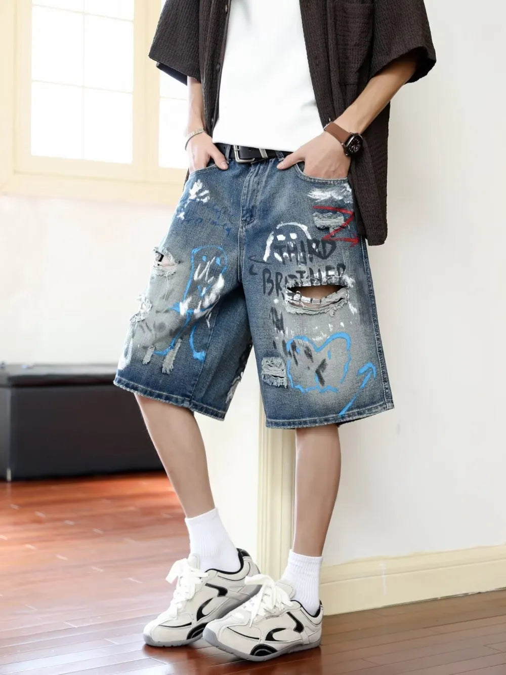 Men's distressed blue denim shorts with graffiti print and ripped details.