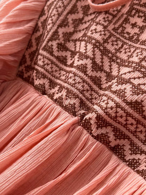 Pink bohemian maxi dress with embroidered V-neck and textured skirt.