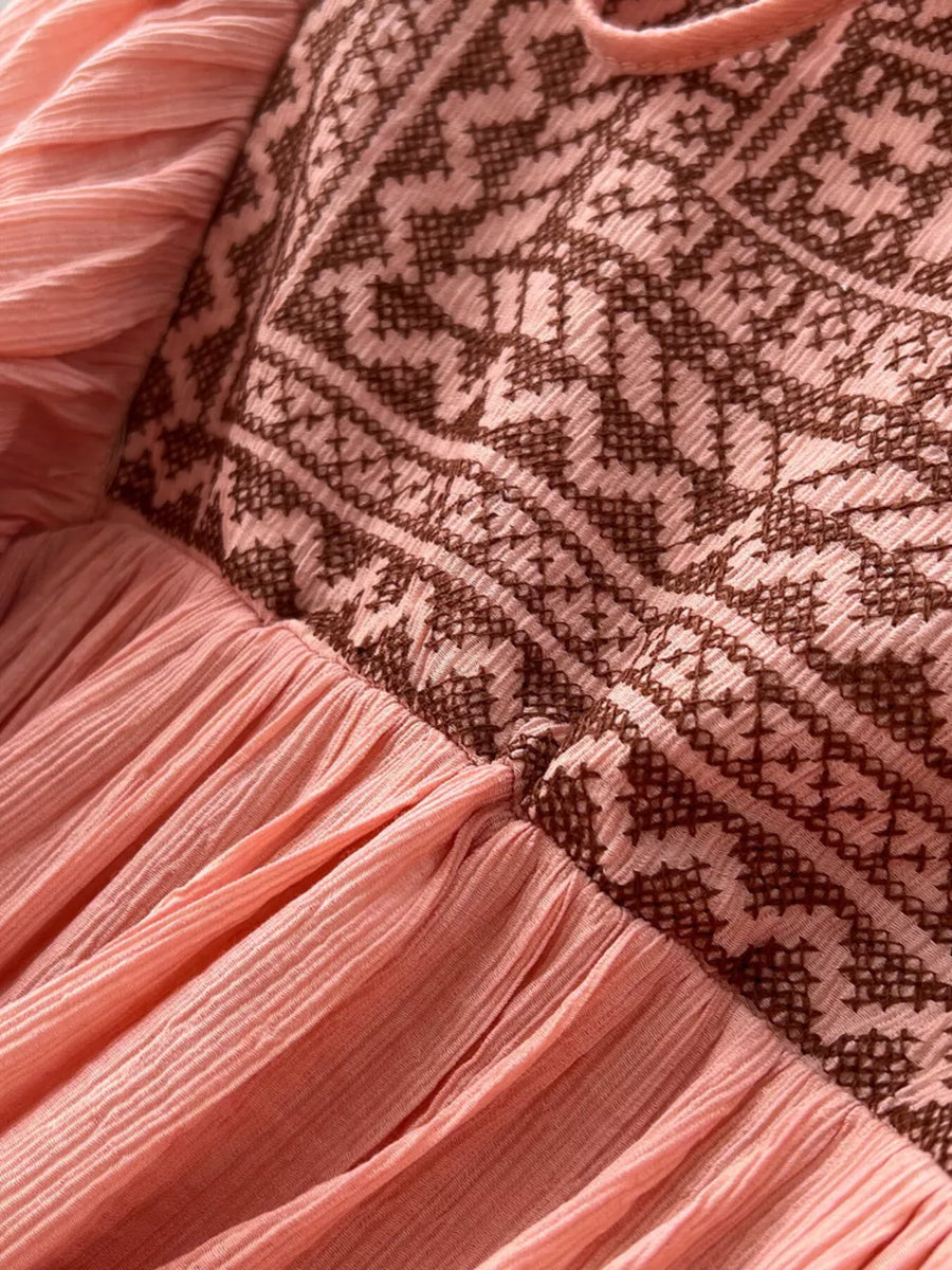 Pink bohemian maxi dress with embroidered V-neck and textured skirt.