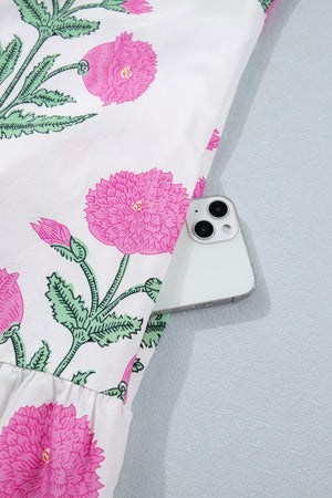 Vibrant floral mini dress with pink flowers and green leaves on white fabric, showing a ruffled hem.