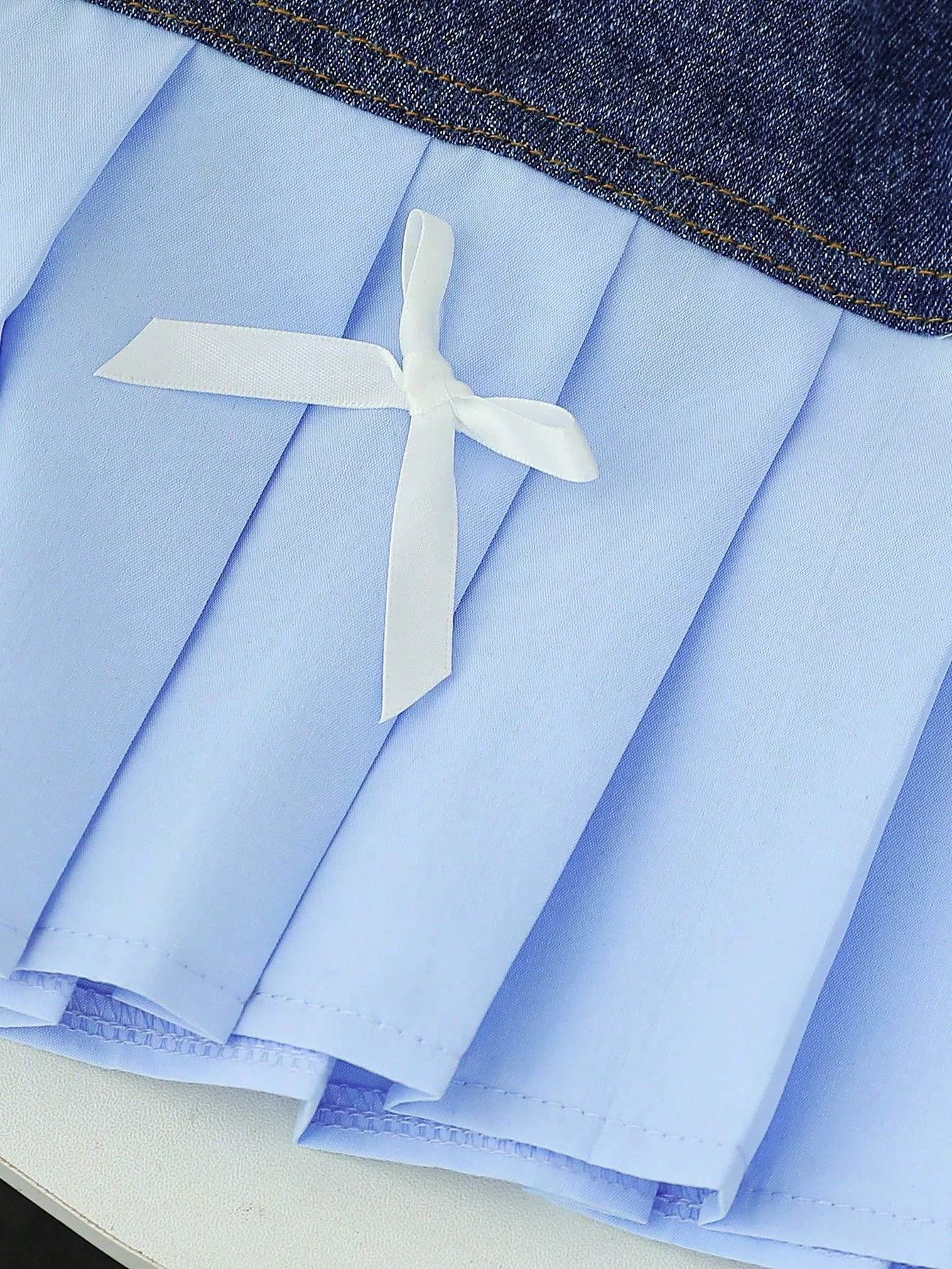 Light blue pleated skirt with denim waistband and white ribbon bow detail.