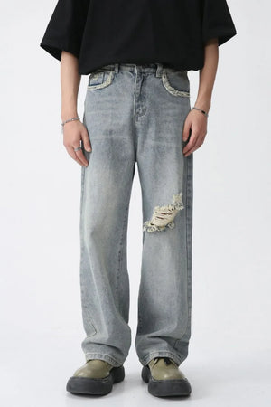Distressed wide-leg denim jeans in medium wash with raw edge pockets and a knee rip.