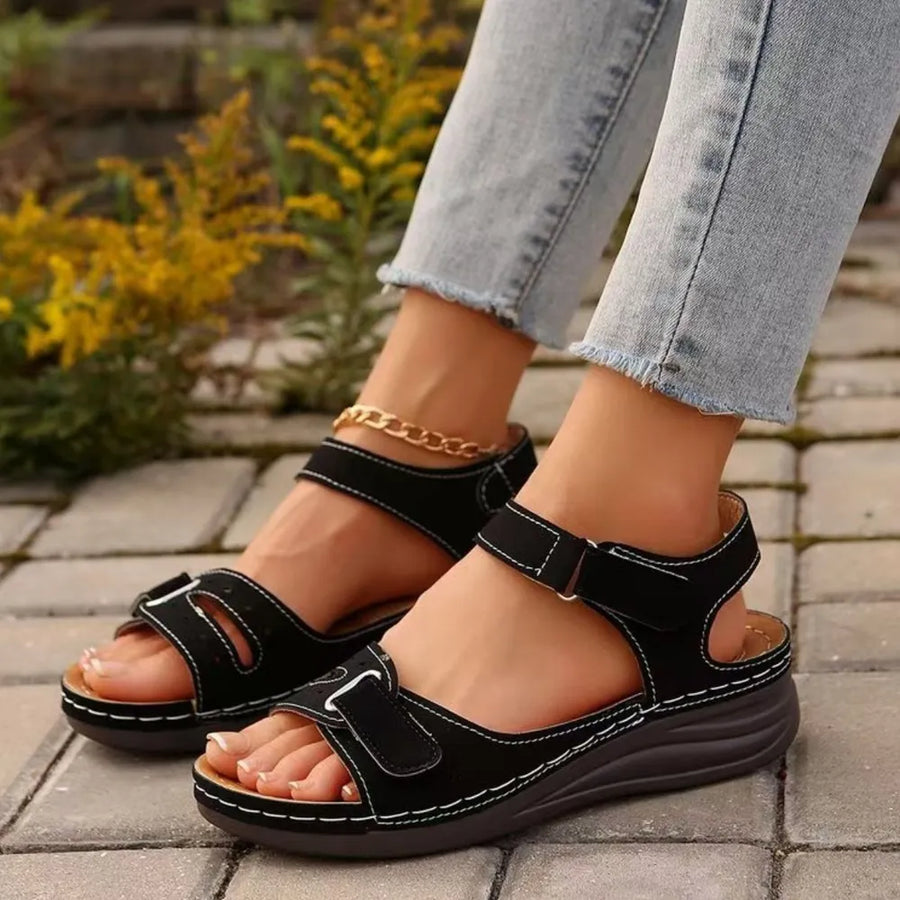 Black perforated detail velcro wedge sandals with white stitching and adjustable straps.