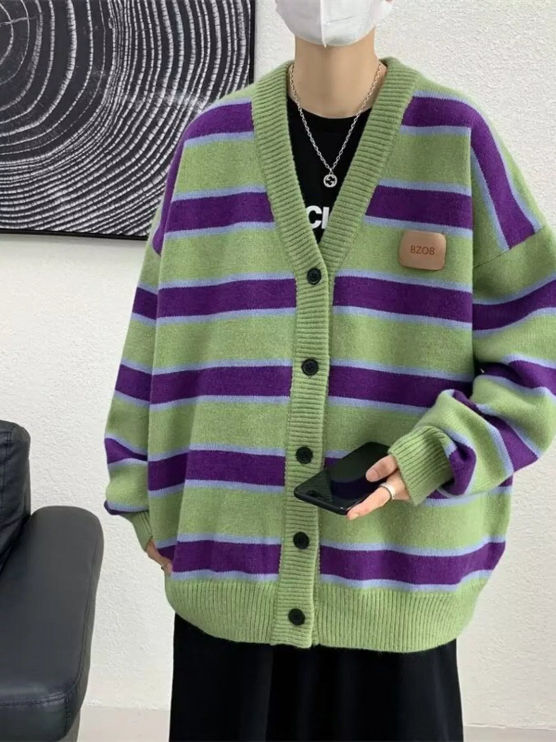 Oversized striped V-neck cardigan in green with purple and light blue stripes, featuring a buttoned front and a faux leather
