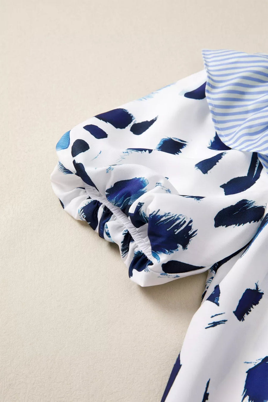 White polyester shirt with blue abstract print, ruffled detail, and striped bow.
