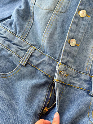 Chic buttoned denim jumpsuit with pockets and zipper detail in light blue cotton fabric.