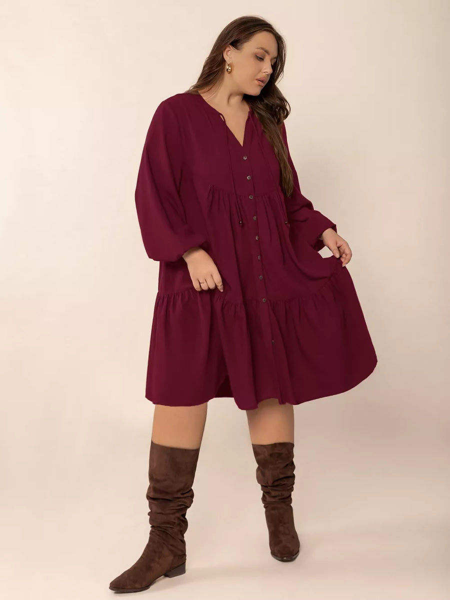 Plus-size burgundy tiered button-front dress with tied V-neck and balloon sleeves.