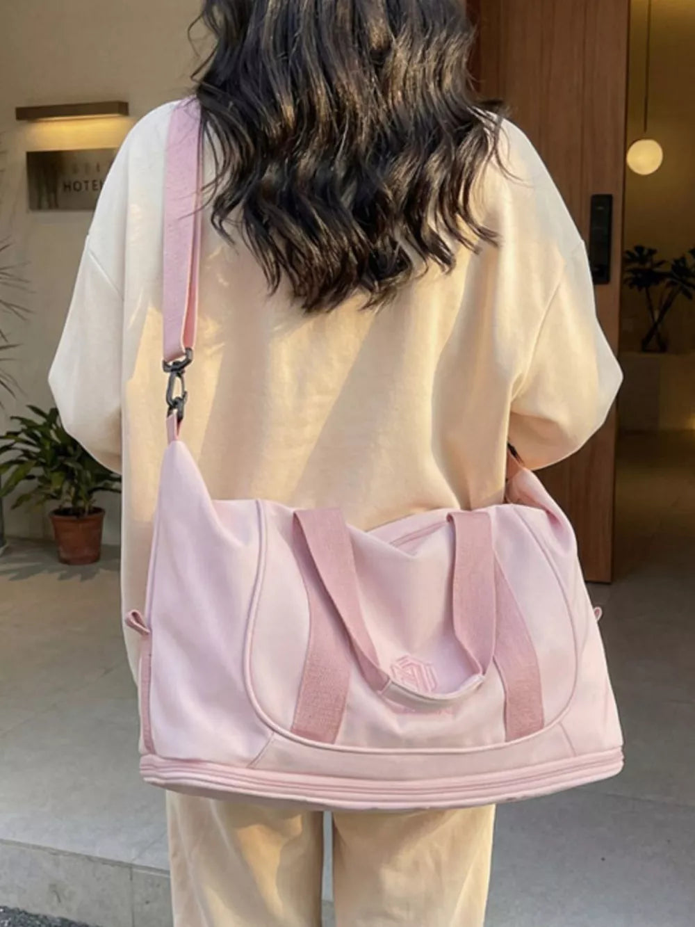 Pink duffel bag with dual handles and adjustable shoulder strap, featuring a subtle embroidered logo.