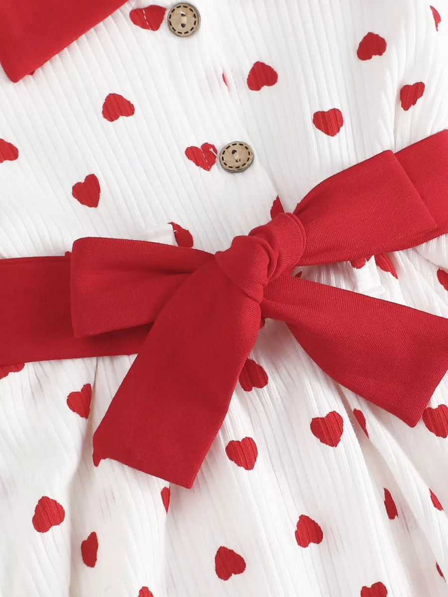 White cotton baby dress with red hearts, red bow belt, and wooden buttons.