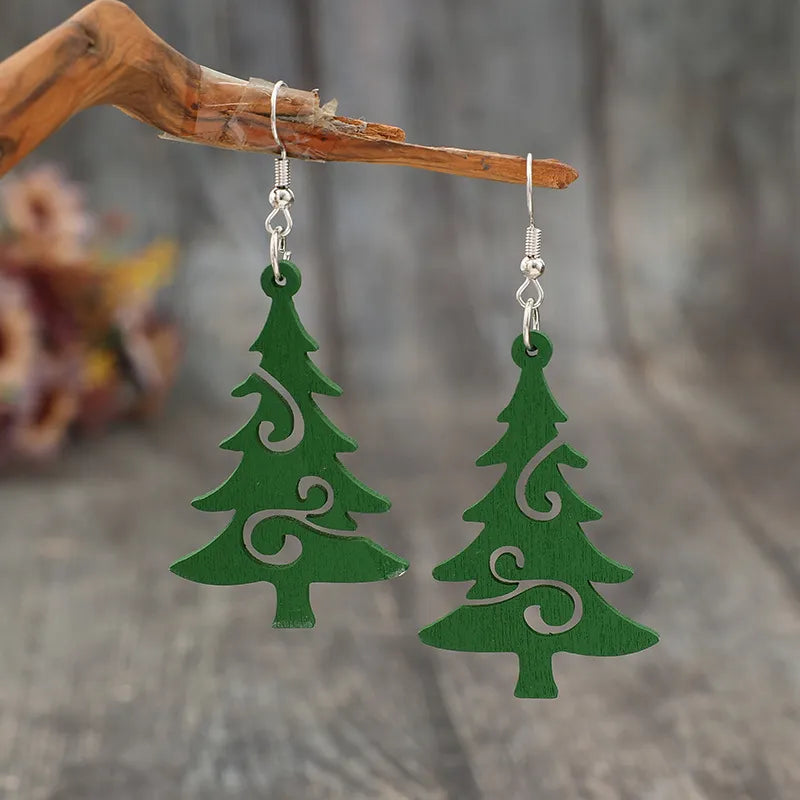Green carved Christmas tree earrings with swirl cutouts, hanging from silver hooks.