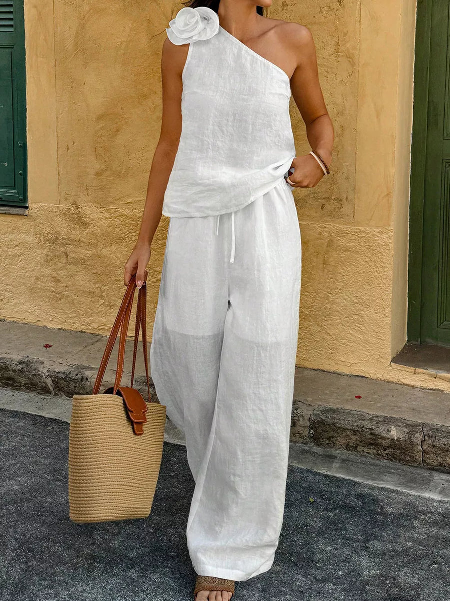 White cotton one-shoulder top with floral embellishment and wide-leg pants.
