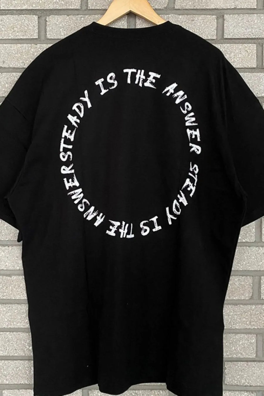 Black oversized t-shirt with white circle text graphic saying "UNSTEADY IS THE ANSWER STEADY IS THE ANSWER