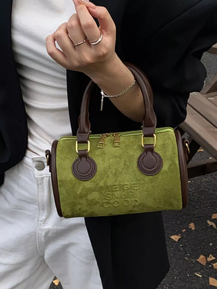 Green suede barrel crossbody bag with brown trim and embossed text detail.